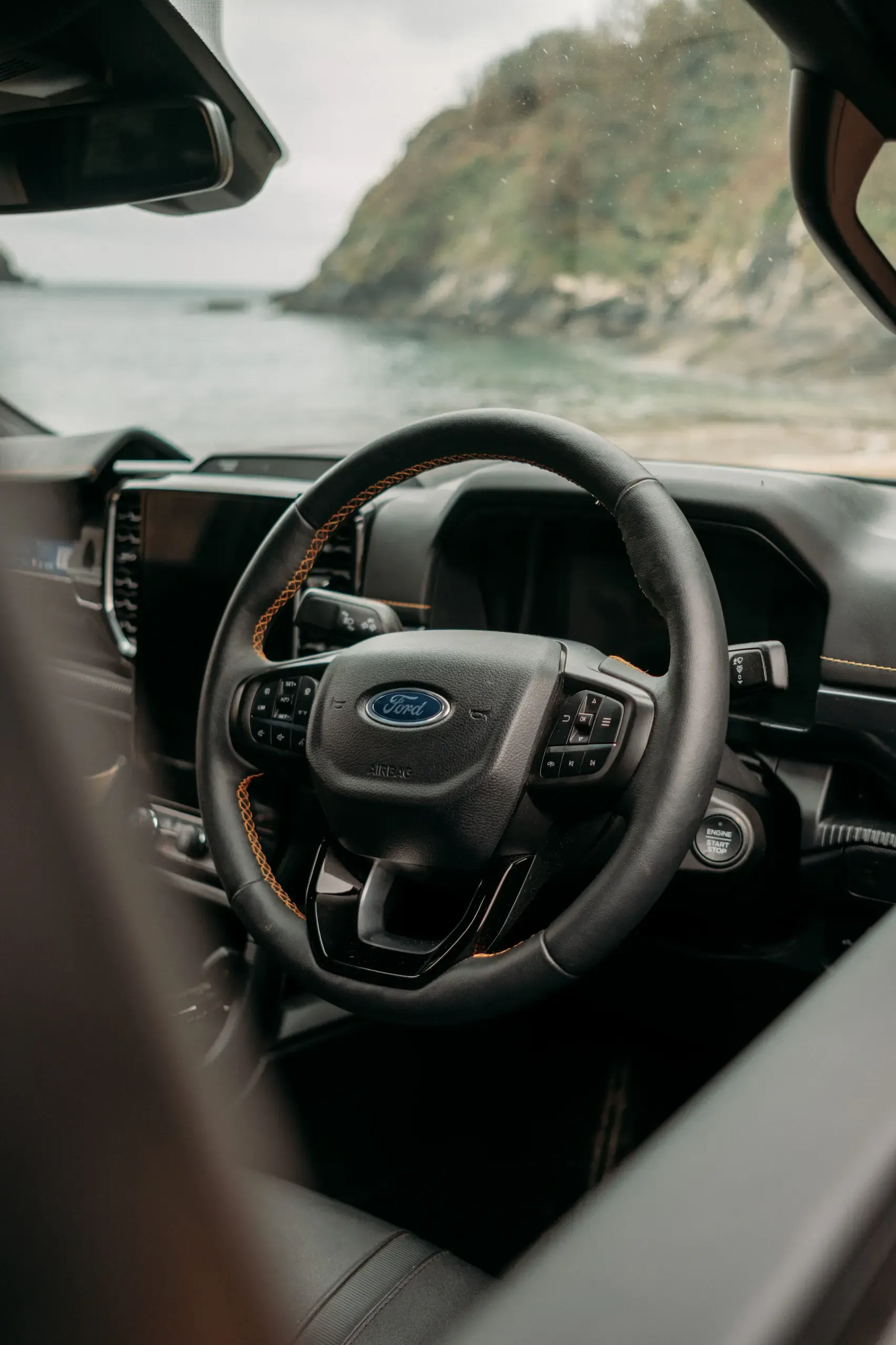 Interior detail of the Ford Ranger Wildtrak dashboard and steering wheel with Cornish coastal headland visible through the windscreen