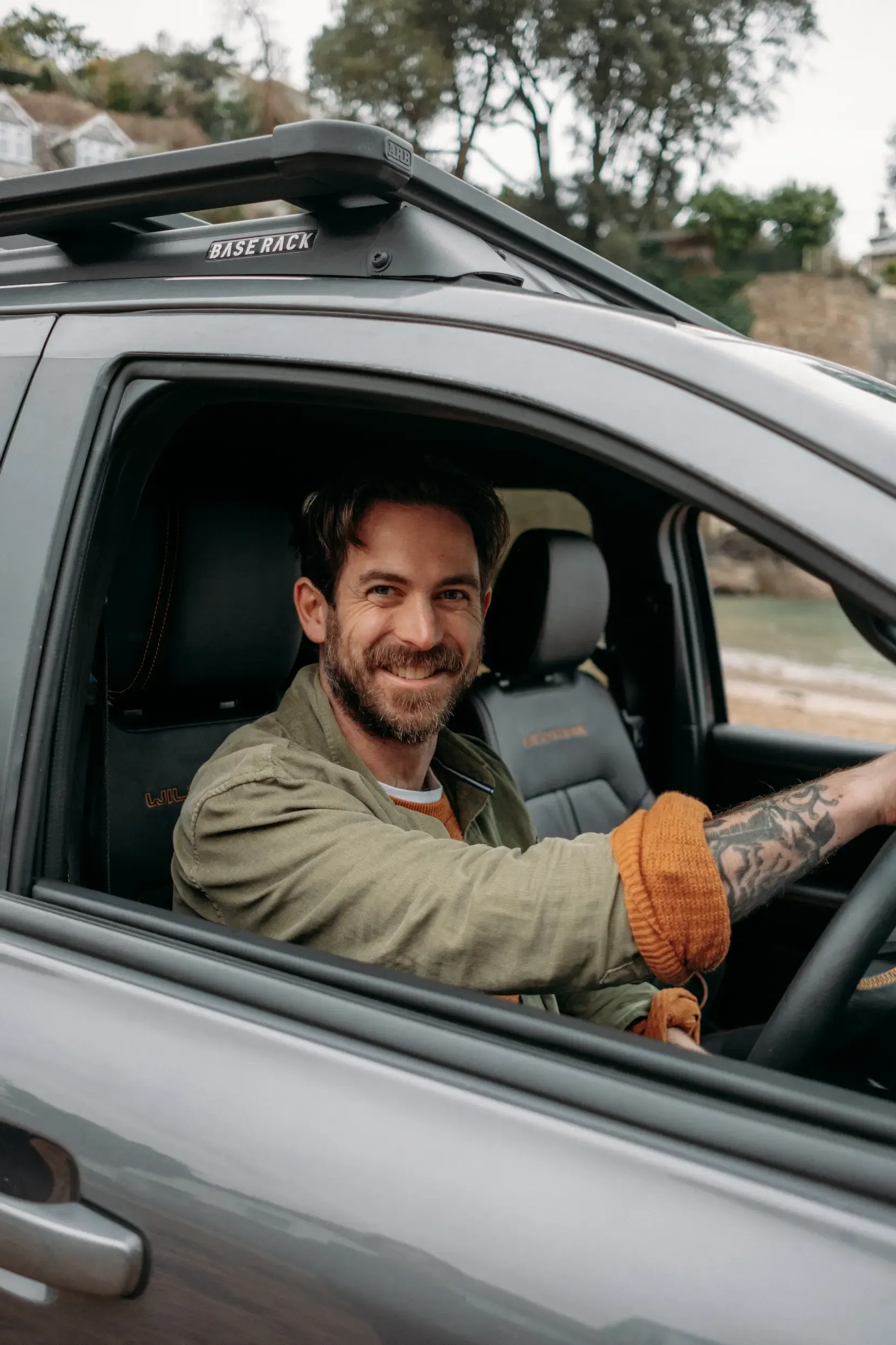 James Strawbridge smiling from the driver's seat of a Ford Ranger Wildtrak with ARB base rack, parked at Readymoney Beach, Fowey, Cornwall