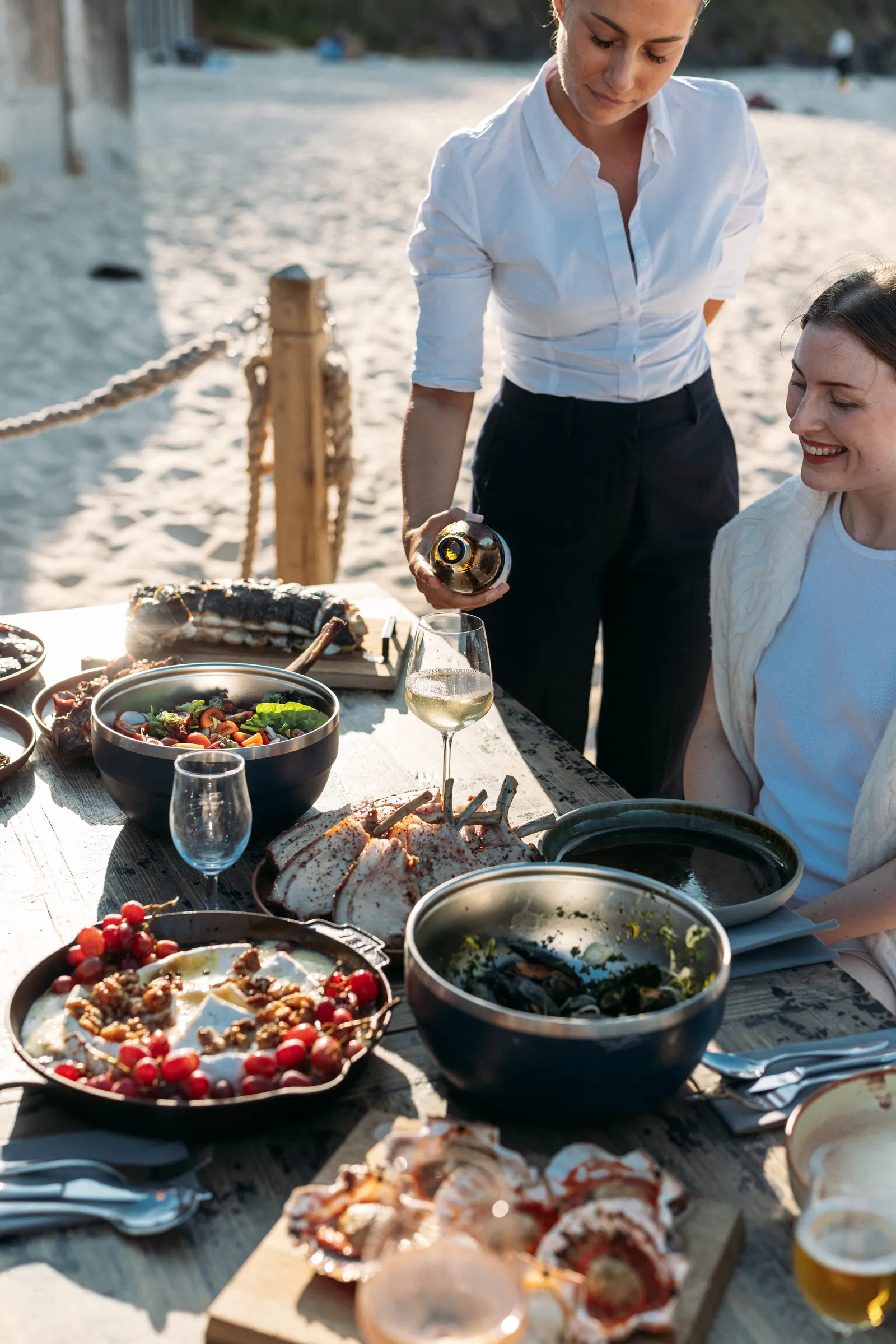 A guest being served wine at a beach barbecue for Carbis Bay Collection