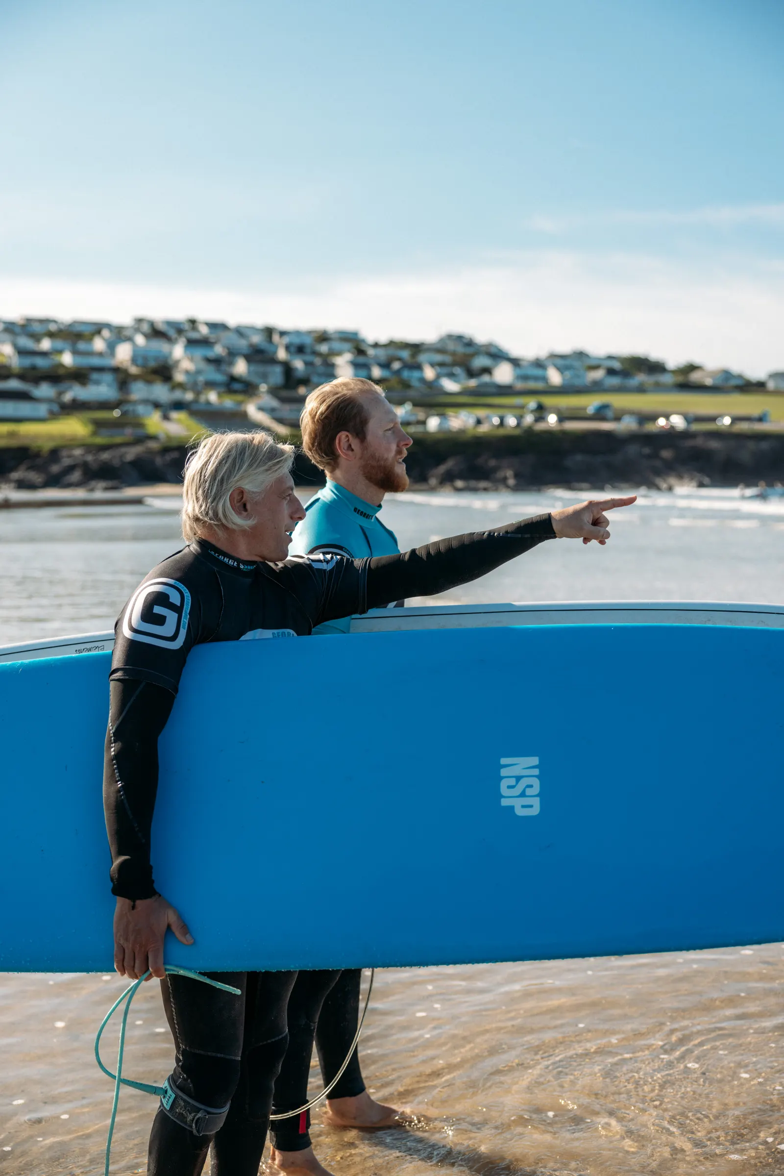 Two surfers carrying a blue surfboard during a Perfect Stays concierge shoot